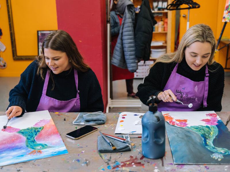 Two friends catch up at a paint and sip class